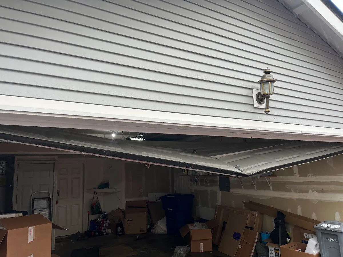 The bottom section of a white garage door bent out of shape and hanging crooked.