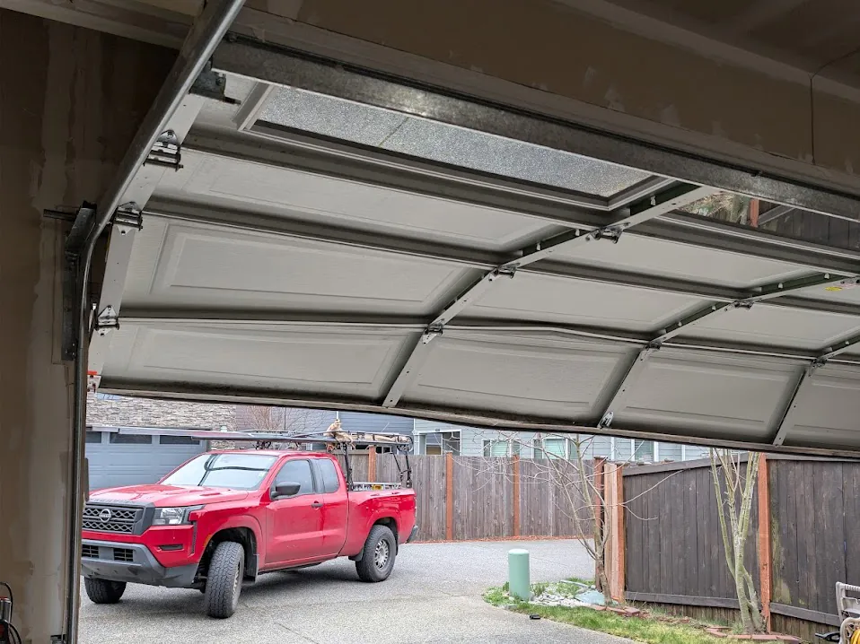 A garage door hanging off its track seen from inside the garage, with the service truck outside.