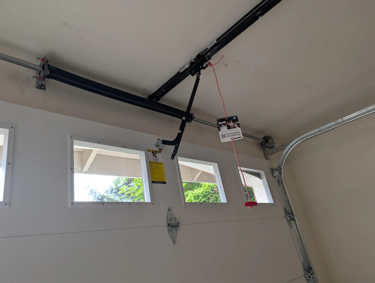 A new torsion spring and opener rail above a white insulated steel garage door with windows.