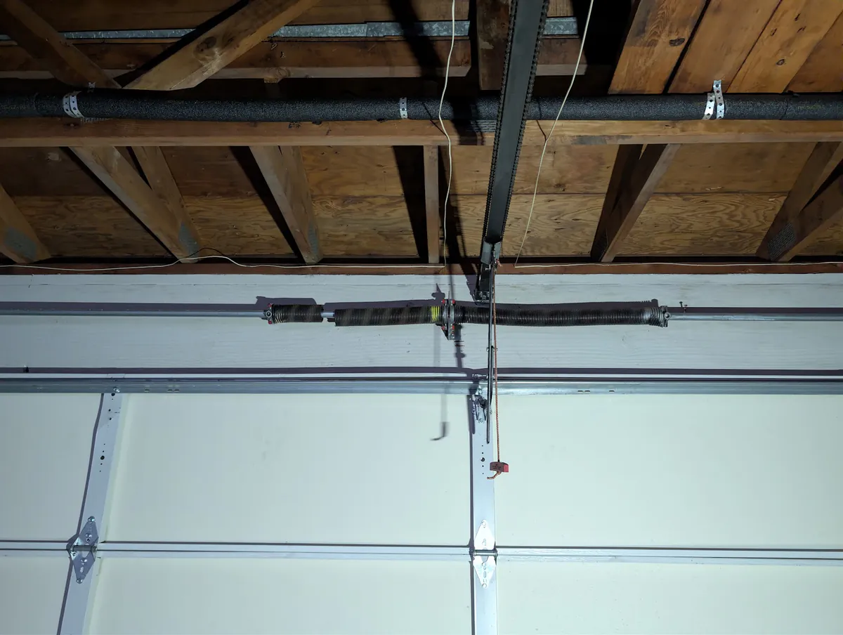A matched pair of torsion springs mounted on a center bracket above a white garage door.