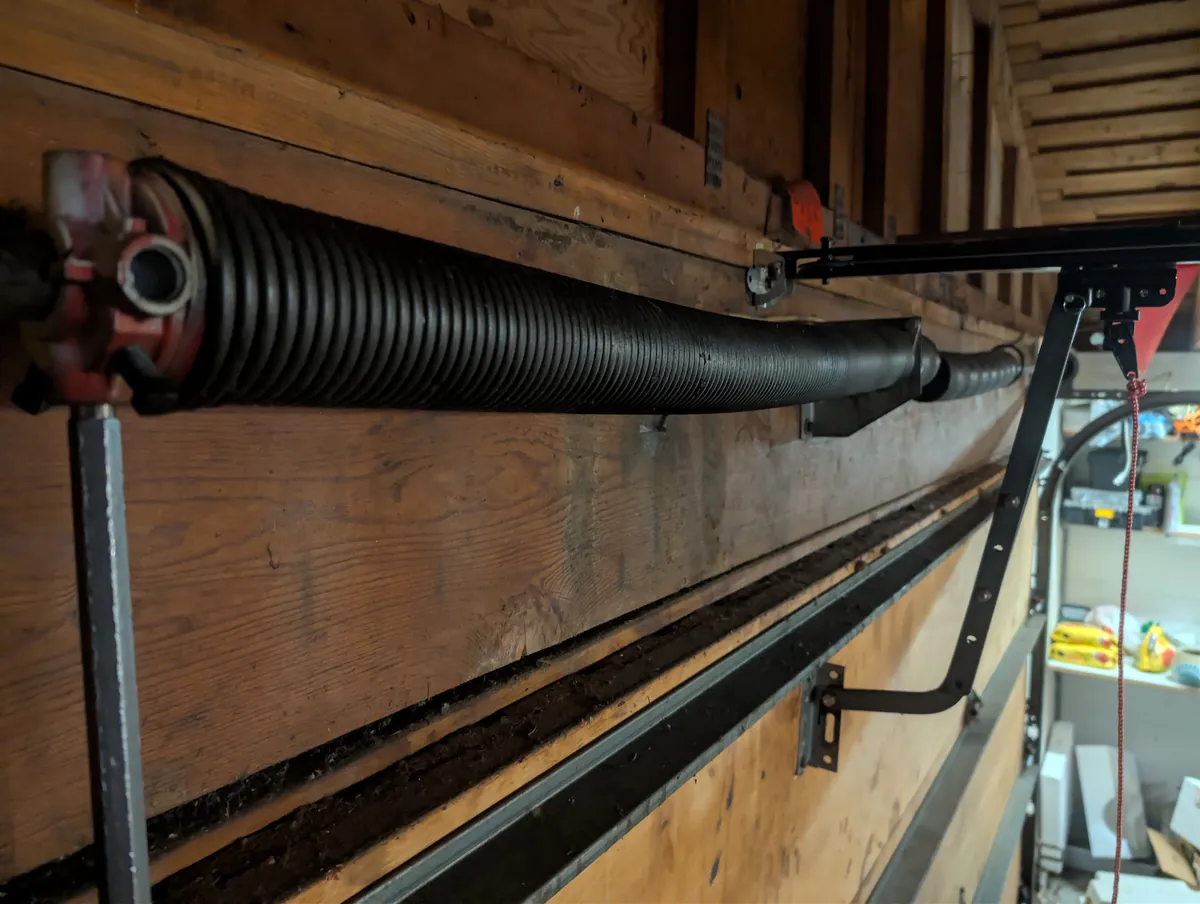Close-up of a torsion spring and red winding cone bolted to the wood header above a garage door.