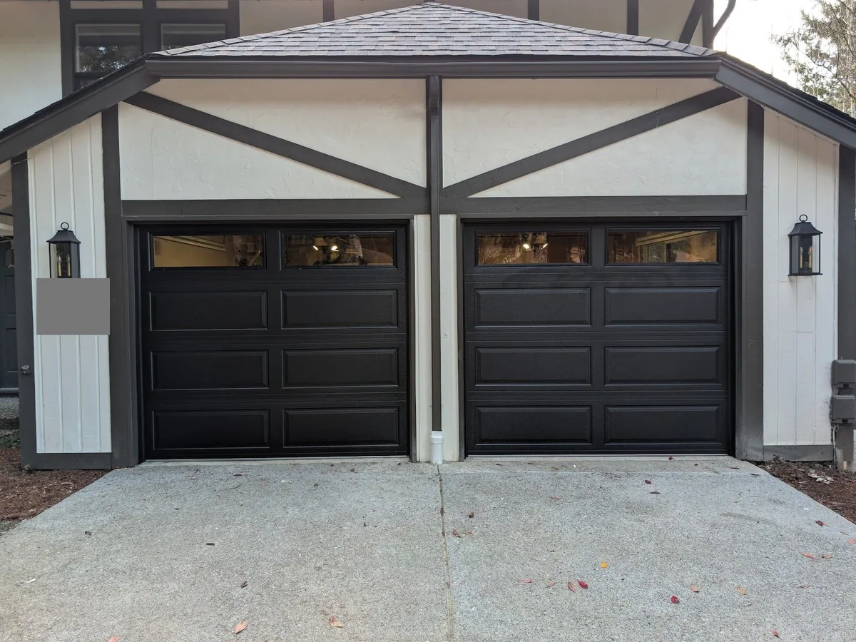 Two black long panel garage doors with window top rows under a timber framed gable