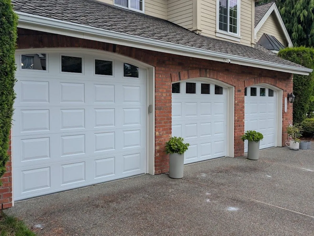 Three white arched carriage style garage doors with window inserts on a brick and cedar home