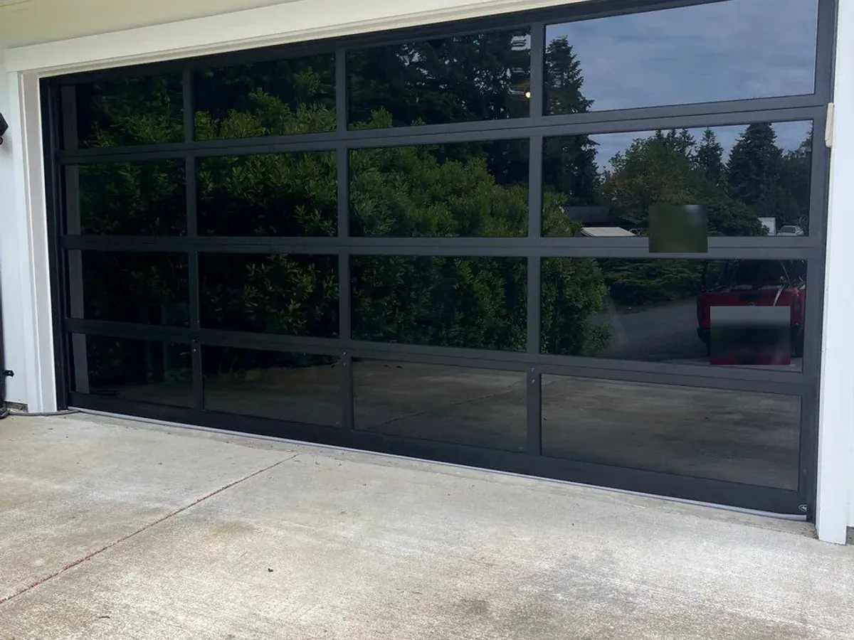 Modern full view garage door with a black aluminum frame and tinted glass panels on a Seattle area home