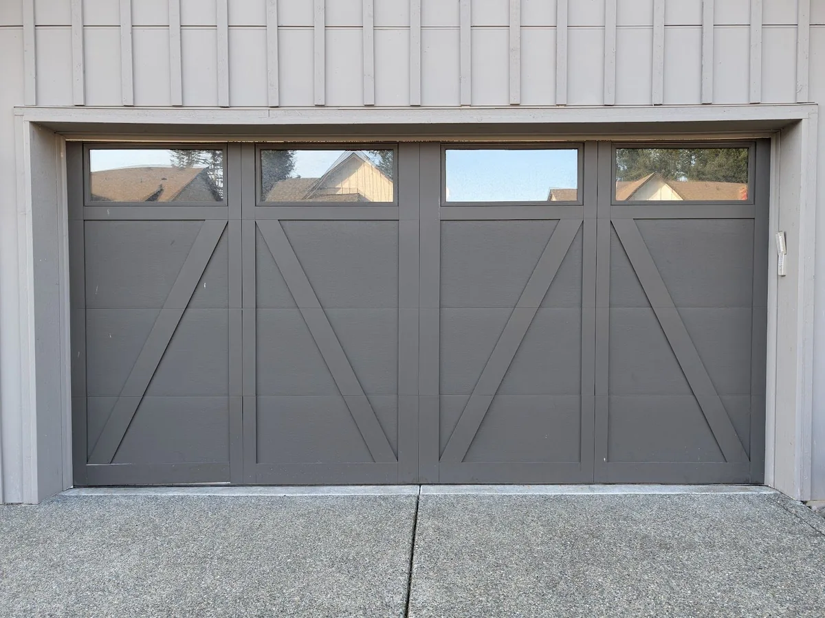 Gray carriage house garage door with cross bracing and four windows across the top