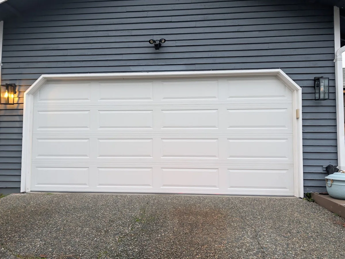 White raised panel garage door on a house with dark charcoal lap siding