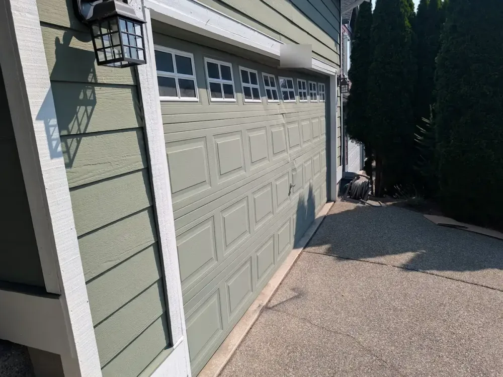 Before: a faded sage green raised-panel garage door in Lynnwood with a crease across the middle sections.